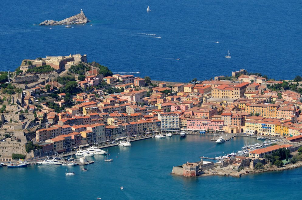 Aerial view of a Tuscan harbour town with fortress, yachts, and terracotta roofs
