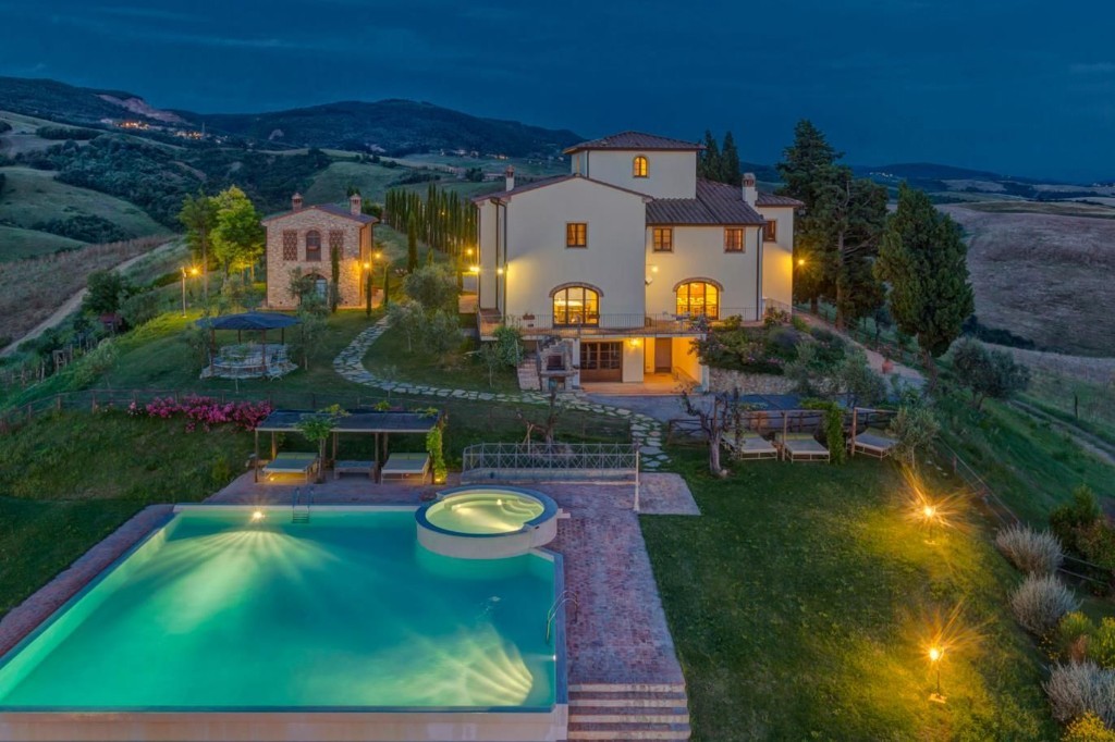 Illuminated Tuscan villa and glowing pool overlooking the countryside at twilight
